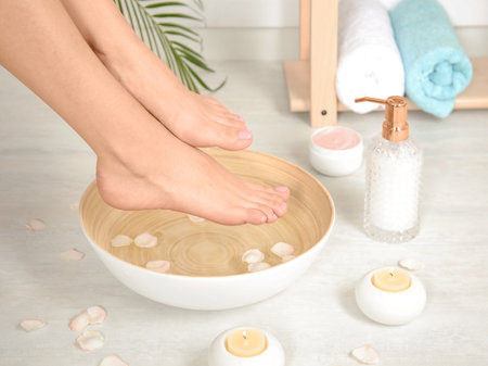 Woman putting her feet into bowl with water and rose petals indoors, closeup. spa treatmentの写真素材