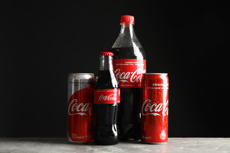 MYKOLAIV, UKRAINE - NOVEMBER 15, 2018: Bottles and cans with Coca Cola on table against black...