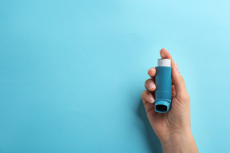 Woman holding asthma inhaler on color background, top view. Space for textの写真素材