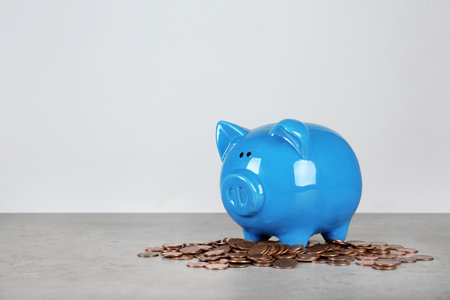Piggy bank and coins on table against white background. Space for textの写真素材