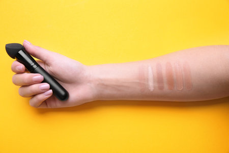 Woman testing different shades of liquid foundation on her hand against color background, closeupの写真素材