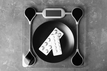 Scales with plate of weight loss pills in blister packs on gray background, top viewの写真素材