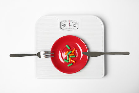Scales with plate of weight loss pills and cutlery on white background, top viewの写真素材