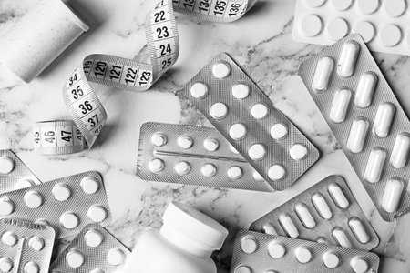 Flat lay composition with weight loss pills and measuring tape on marble backgroundの写真素材