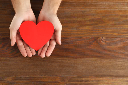 Man holding paper heart on wooden background, top view with space for textの写真素材
