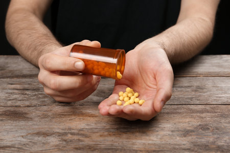 Man pouring pills out of bottle into hand at table, closeupの写真素材