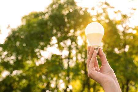 Woman holding lamp bulb outdoors, closeup. Space for text