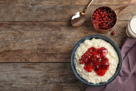 Creamy rice pudding with red currant and jam in bowl served on wooden table, top view. Space for textの写真素材