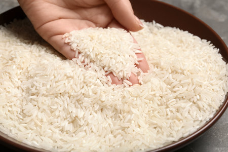 Woman holding grains near plate with rice on table, closeupの写真素材