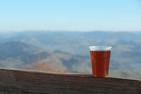 Plastic cup of natural hot tea on wooden railing in mountains. Space for textの写真素材