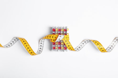 Weight loss pills in blister packs tied with measuring tape on white background, top viewの写真素材
