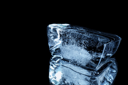 Ice cube on black mirror surface. Space for textの写真素材