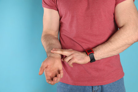 Young man checking pulse on color background, closeupの写真素材