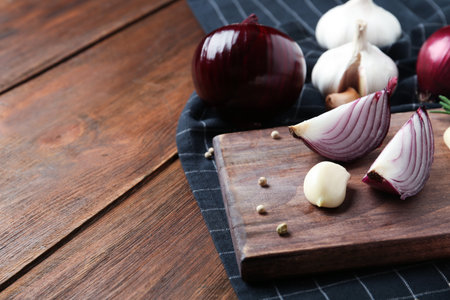 Board with cut onion and garlic clove on wooden table. Space for textの写真素材