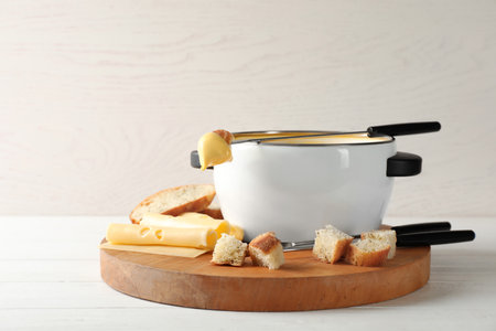 Pot of delicious cheese fondue and fork with bread on wooden tableの写真素材