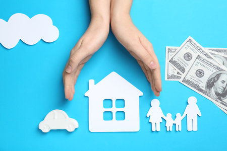 Woman holding hands over paper silhouettes of family, house and car on color background, top view. life insurance conceptの写真素材