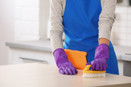 Woman cleaning table with brush in kitchen, closeup. Space for textの写真素材