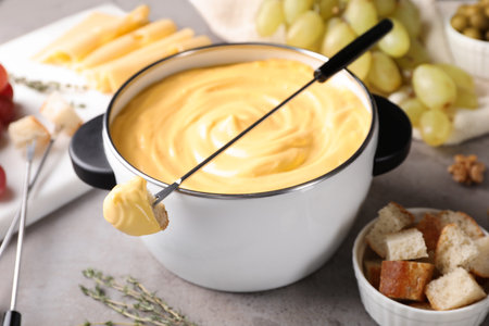 Pot of delicious cheese fondue and fork with bread on gray tableの写真素材