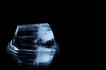 Ice cube on black mirror surface. Space for textの写真素材