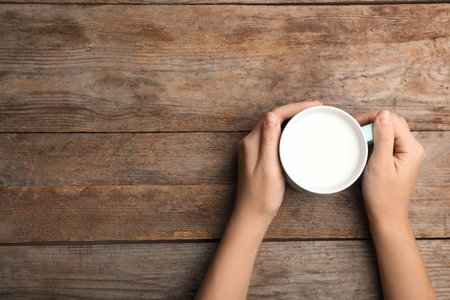 Woman holding cup of milk on wooden table, top view. Space for textの写真素材