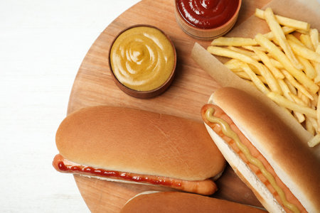 Composition with hot dogs, french fries and sauce on wooden board, top viewの写真素材