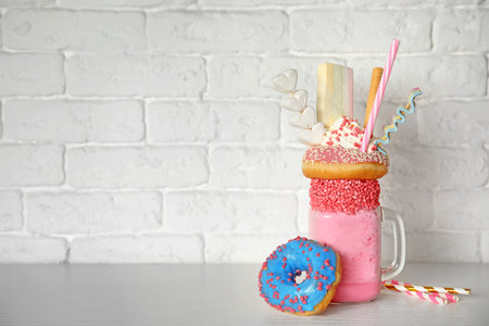 Mason jar of tasty milk shake with sweets on table near brick wall. Space for textの写真素材
