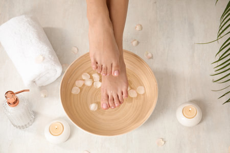 Woman holding her feet over bowl with water and rose petals on floor, closeup. spa treatmentの写真素材