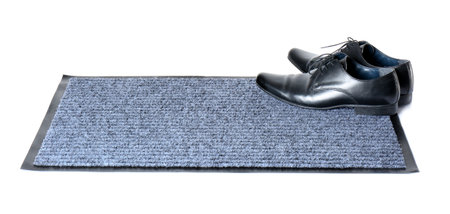 Black classic shoes on gray doormat against white backgroundの写真素材