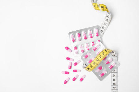 Weight loss pills and measuring tape on white background, top view. Space for textの写真素材