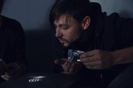 Young addicted men taking drugs on gray background