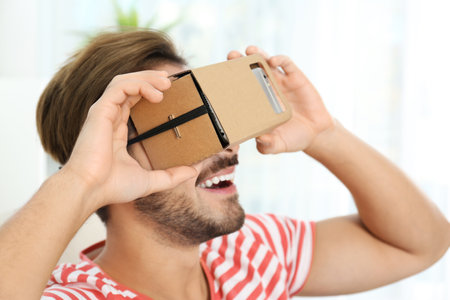 Young man using cardboard virtual reality headset at homeの写真素材