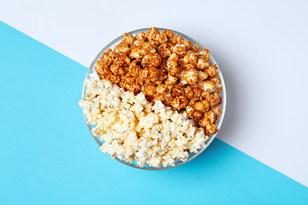 Different kinds of popcorn in bowl on color background, top viewの写真素材