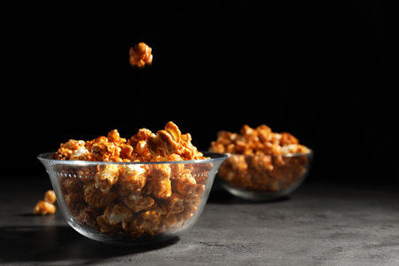 Tasty popcorn falling into bowl on table against black background. Space for textの写真素材