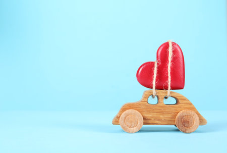 Red decorative heart tied to wooden toy car on color background. Space for textの写真素材