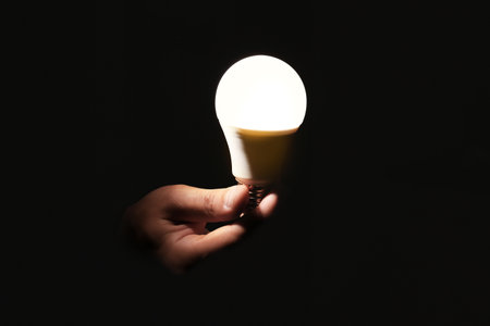 Man holding modern lamp bulb on dark background, closeupの写真素材