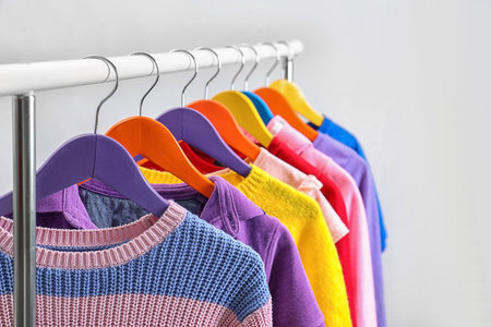 Colorful clothes hanging on wardrobe rack against light background, closeupの写真素材