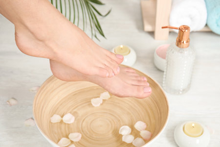 Woman putting her feet into bowl with water and rose petals indoors, closeup. spa treatmentの写真素材