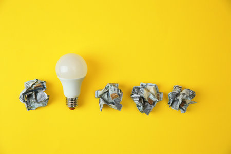 Flat lay composition with lamp bulb and crumpled money on color background