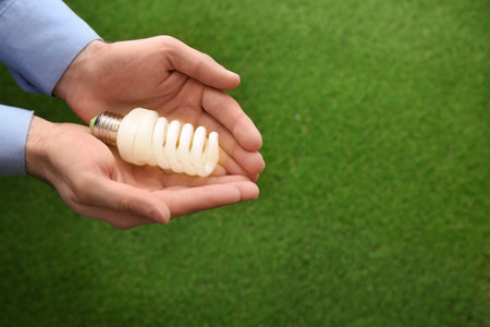 Man holding energy saving bulb for lamp over green grass, closeup. Space for textの写真素材