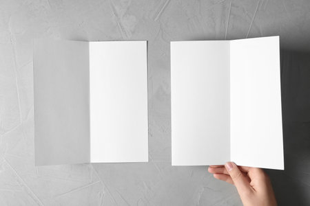Woman with blank brochures on gray background, top view. Mockup for designの写真素材
