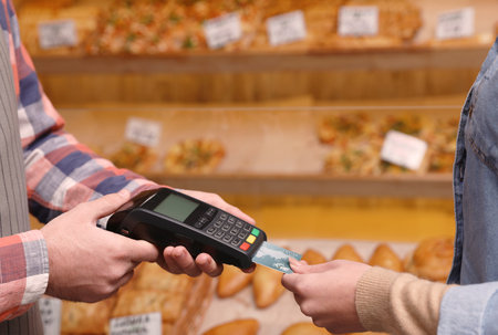 Woman using credit card for terminal payment in bakery, closeup. Space for textの写真素材