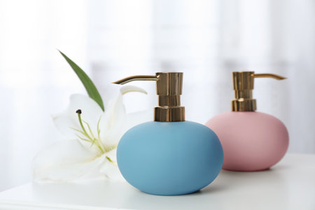 Stylish soap dispensers and lily on table against blurred background. Space for textの写真素材