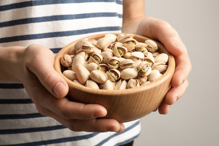 Woman holding bowl with pistachio nuts on light background, closeupの写真素材