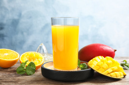 Glass of fresh mango drink and tropical fruits on table against color backgroundの写真素材