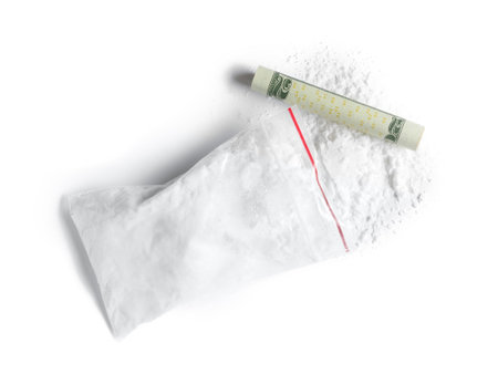 Cocaine in plastic bag and rolled money bill on white background, top view