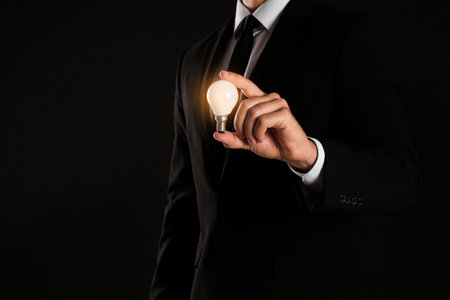 Businessman holding lamp against dark background, closeup. Space for textの写真素材