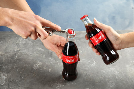 MYKOLAIV, UKRAINE - NOVEMBER 15, 2018: People with bottles of Coca Cola at table, closeup