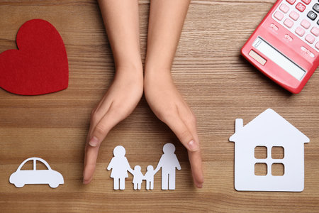 Woman holding hands over paper silhouette of family on wooden background, top view. life insurance conceptの写真素材