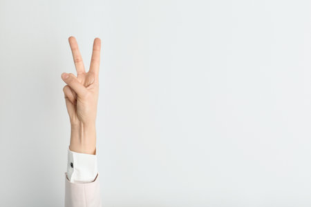 Young woman showing victory gesture on light background. Space for textの写真素材