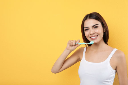 Beautiful woman brushing teeth on color background. Space for textの写真素材